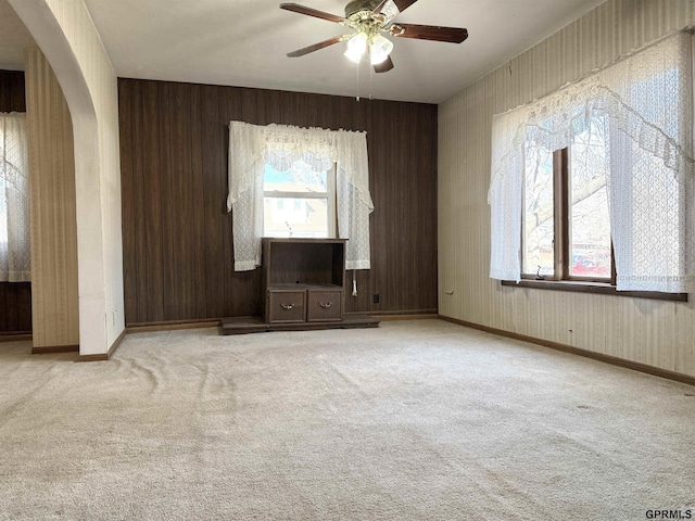 carpeted spare room with arched walkways, ceiling fan, and baseboards