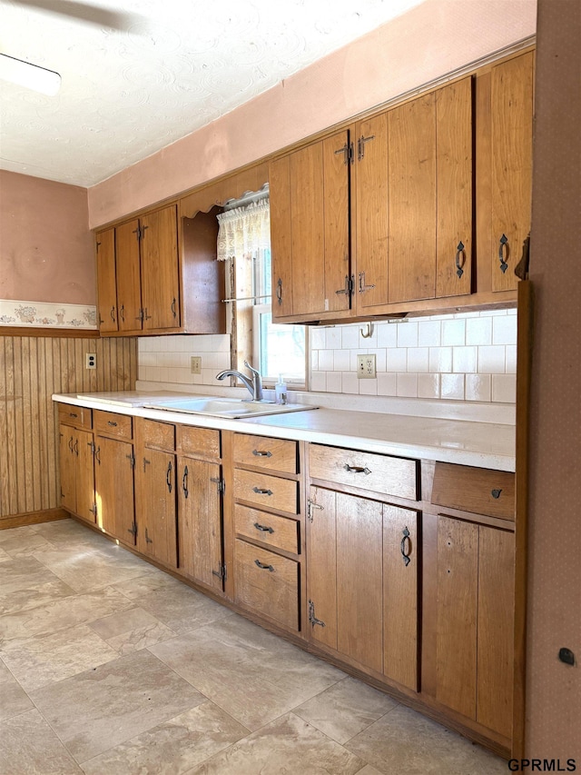 kitchen featuring light countertops, wainscoting, a sink, and brown cabinets