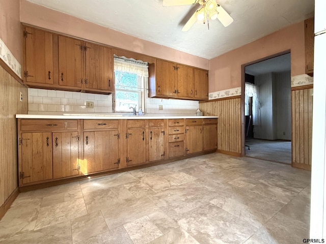 kitchen with wainscoting, ceiling fan, brown cabinets, light countertops, and a sink