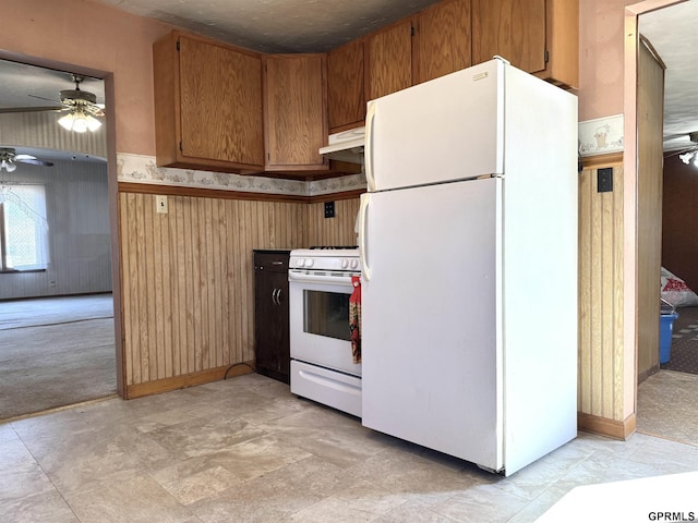 kitchen with white appliances, ceiling fan, brown cabinets, wood walls, and under cabinet range hood