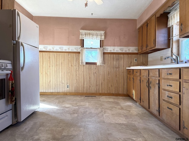 kitchen with white appliances, wood walls, light countertops, wainscoting, and brown cabinetry