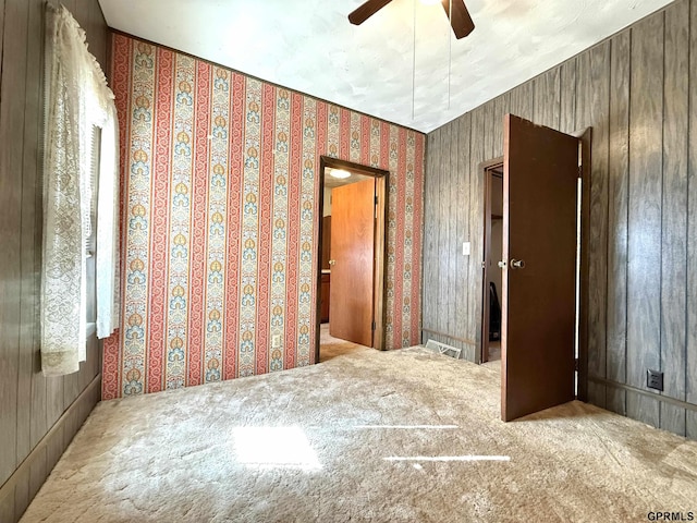 carpeted spare room featuring wallpapered walls and a ceiling fan