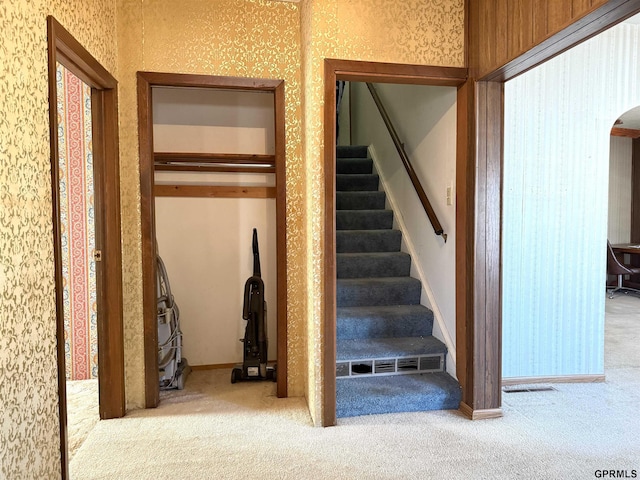 stairway with arched walkways, carpet floors, baseboards, and wallpapered walls