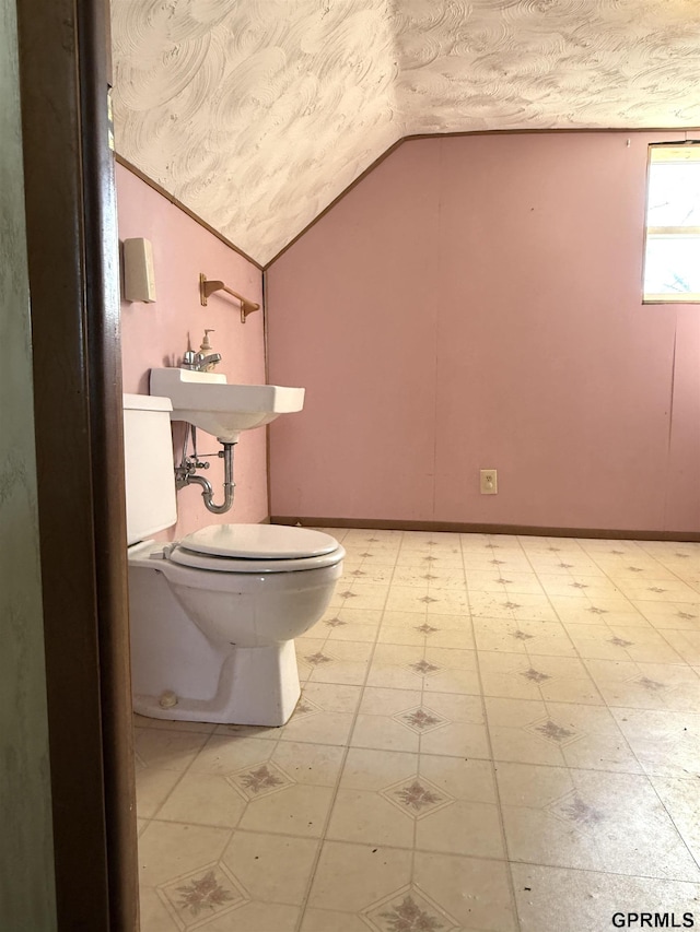 half bathroom with lofted ceiling, a textured ceiling, toilet, baseboards, and tile patterned floors