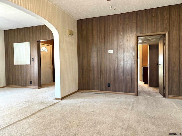 unfurnished room featuring arched walkways, light colored carpet, a textured ceiling, and baseboards