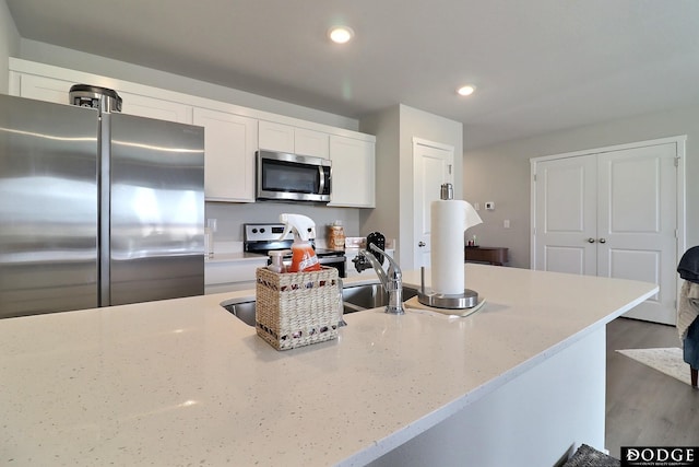 kitchen featuring white cabinets, appliances with stainless steel finishes, wood finished floors, light stone countertops, and recessed lighting