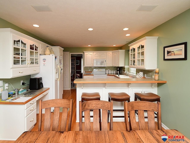 kitchen featuring a breakfast bar, range with electric stovetop, white microwave, glass insert cabinets, and a peninsula