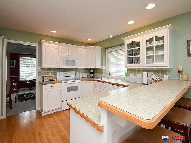 kitchen featuring a breakfast bar, glass insert cabinets, white cabinetry, a sink, and white appliances