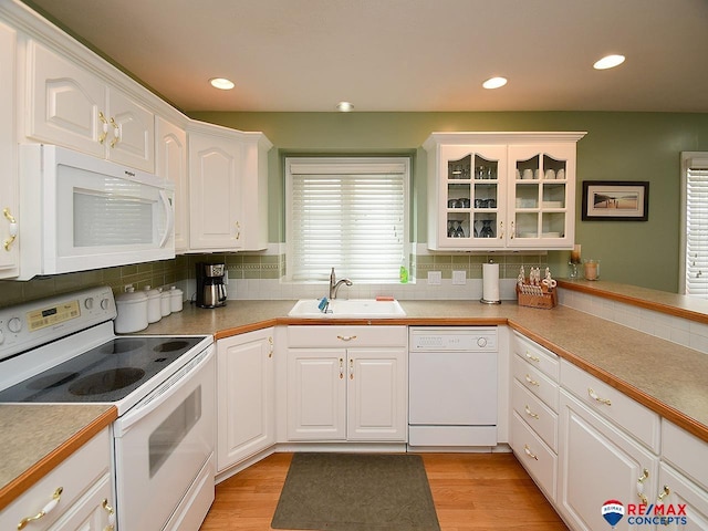 kitchen featuring white appliances, light wood-type flooring, a sink, and white cabinetry