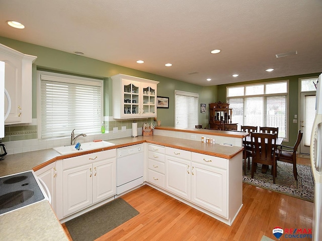 kitchen featuring light wood-style flooring, white cabinetry, white dishwasher, a sink, and a peninsula