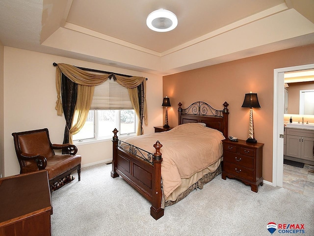 bedroom with light carpet, a sink, baseboards, a raised ceiling, and ensuite bath