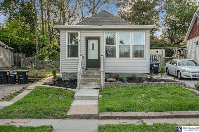 bungalow-style house with entry steps, roof with shingles, and a front yard