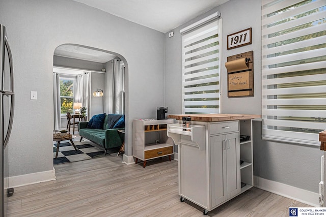 office space with arched walkways, a textured wall, light wood finished floors, and baseboards