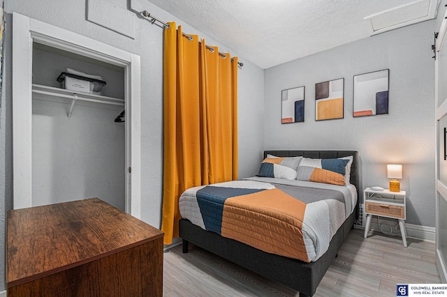 bedroom featuring attic access, baseboards, light wood-style flooring, a textured ceiling, and a closet