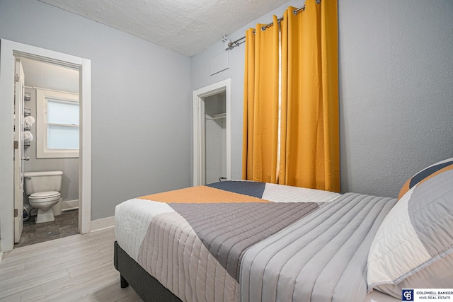 bedroom with a closet, light wood-style flooring, connected bathroom, a textured ceiling, and baseboards