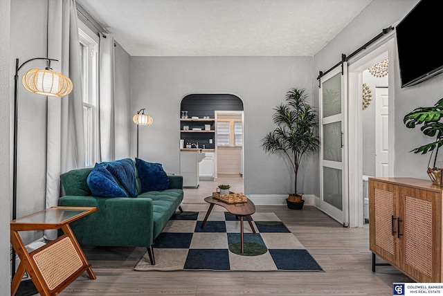 living room featuring arched walkways, a barn door, wood finished floors, and baseboards