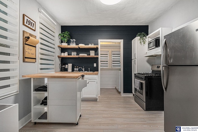 kitchen with wood counters, stainless steel appliances, light wood-type flooring, white cabinetry, and open shelves