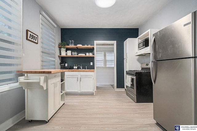 kitchen featuring stainless steel appliances, butcher block counters, white cabinetry, light wood-style floors, and open shelves