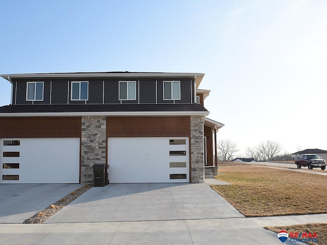 view of front facade featuring an attached garage, stone siding, concrete driveway, and a front yard