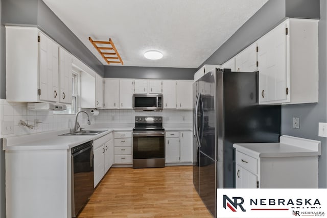 kitchen with stainless steel appliances, a sink, white cabinets, light wood-style floors, and backsplash