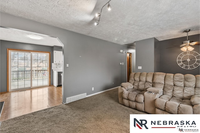 living area featuring arched walkways, ceiling fan, carpet floors, visible vents, and baseboards