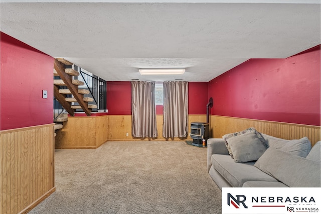 carpeted living room with a textured ceiling, a wainscoted wall, wood walls, stairway, and a wood stove