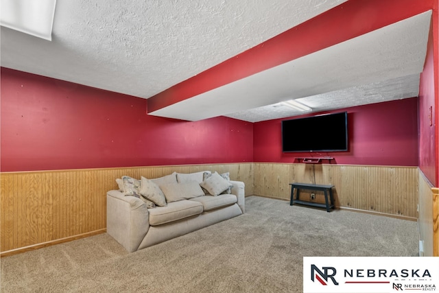 carpeted living room featuring wainscoting, wood walls, and a textured ceiling