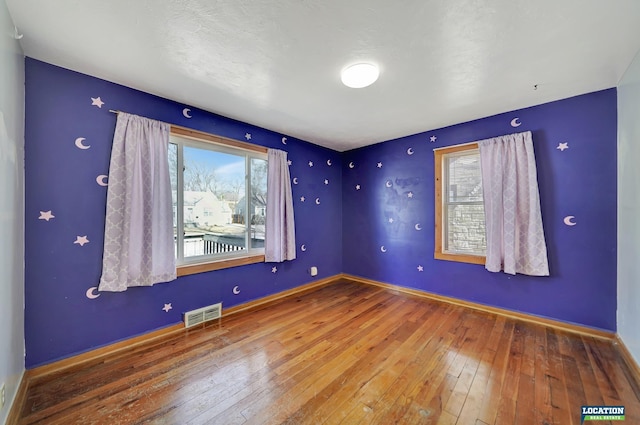 empty room with baseboards, visible vents, and hardwood / wood-style floors