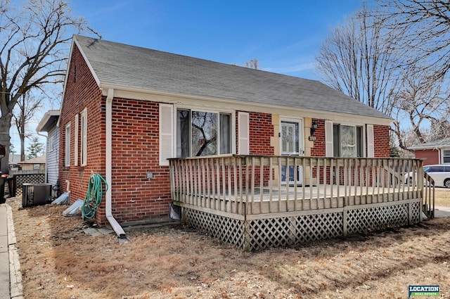 view of front of house featuring a shingled roof, cooling unit, brick siding, and a deck