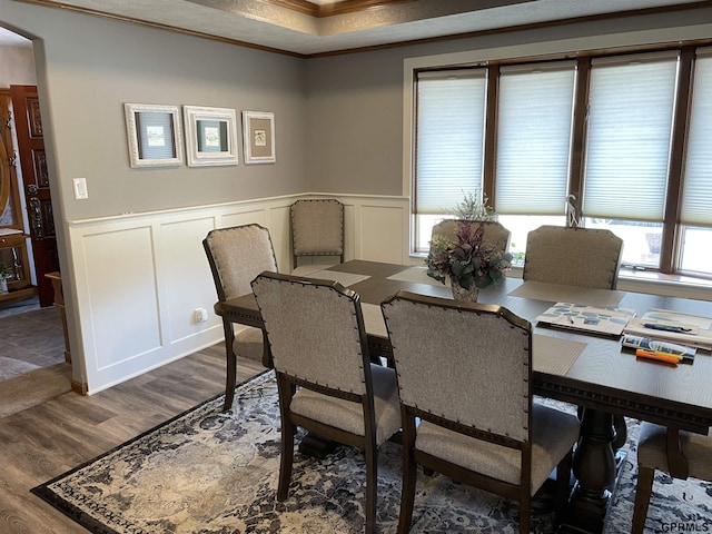 dining area with a wainscoted wall, ornamental molding, wood finished floors, and a decorative wall