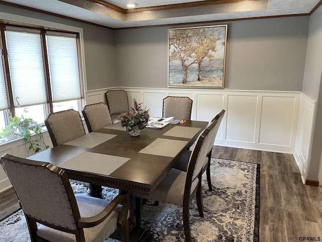 dining area with dark wood-style flooring, crown molding, a raised ceiling, a decorative wall, and wainscoting