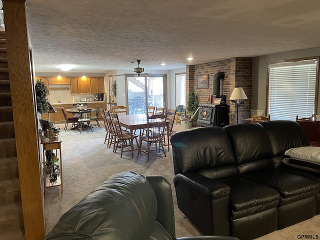 living area featuring light carpet, ceiling fan, a textured ceiling, and a wood stove