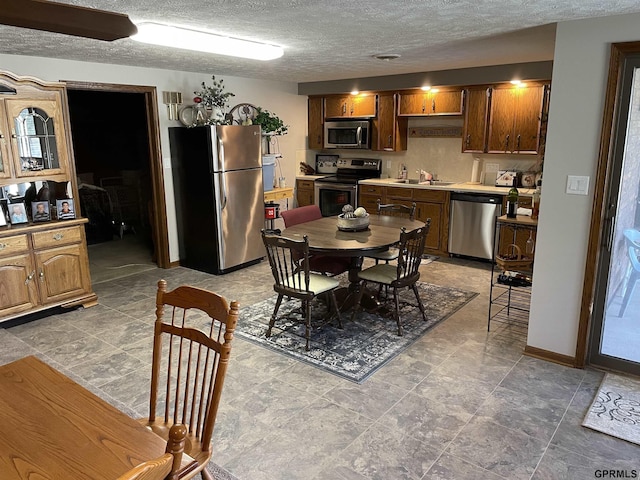 kitchen with appliances with stainless steel finishes, a sink, a textured ceiling, and baseboards