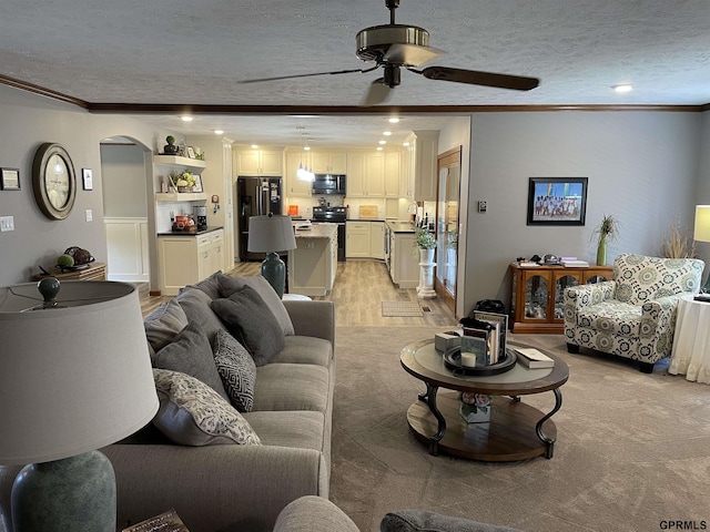 living area with a textured ceiling, ornamental molding, light wood finished floors, and arched walkways