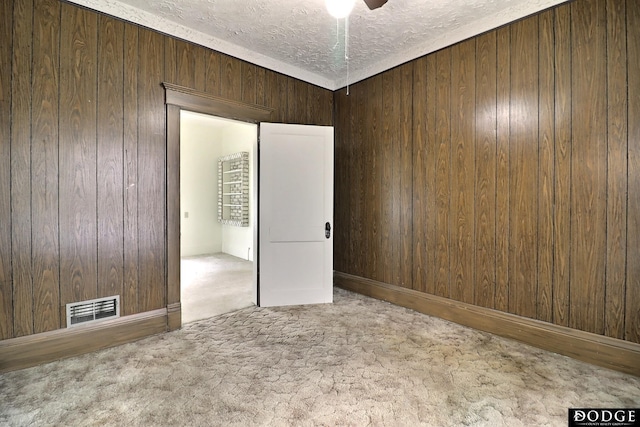 carpeted spare room featuring visible vents, wooden walls, and a textured ceiling