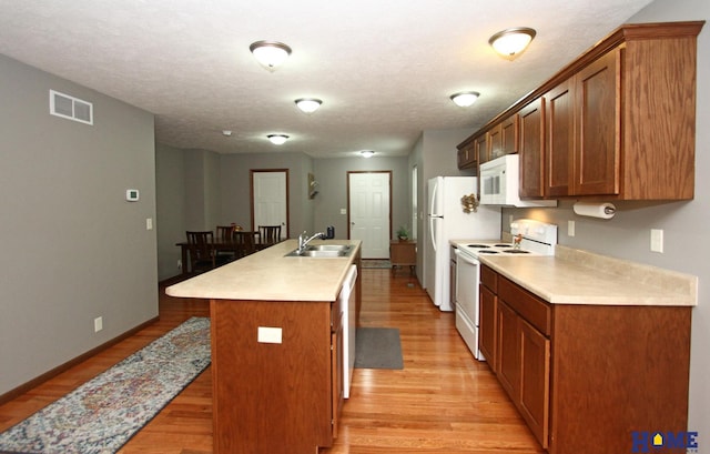 kitchen with white appliances, a sink, visible vents, light wood finished floors, and a center island with sink