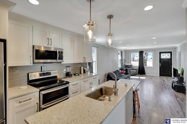 kitchen with white cabinets, decorative backsplash, wood finished floors, stainless steel appliances, and a sink