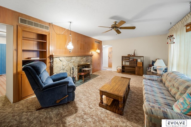 carpeted living area with a stone fireplace, wooden walls, built in shelves, and visible vents