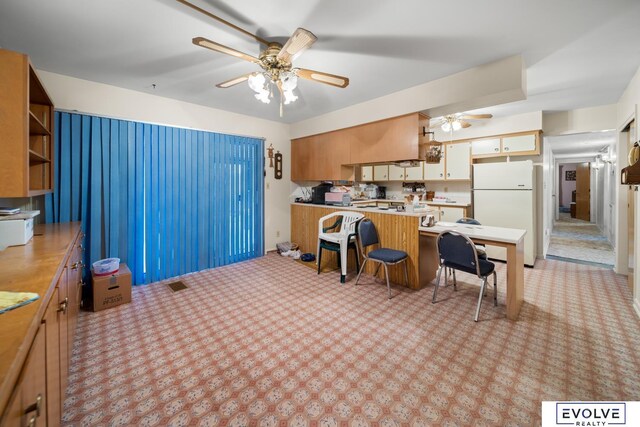 kitchen featuring a ceiling fan, visible vents, a peninsula, freestanding refrigerator, and light countertops