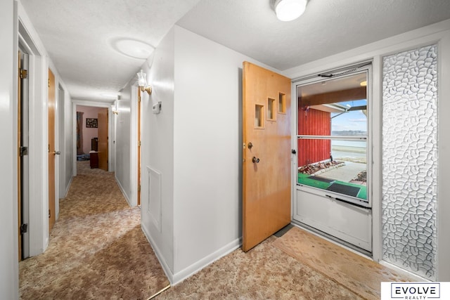 hallway featuring baseboards, a textured ceiling, and carpet