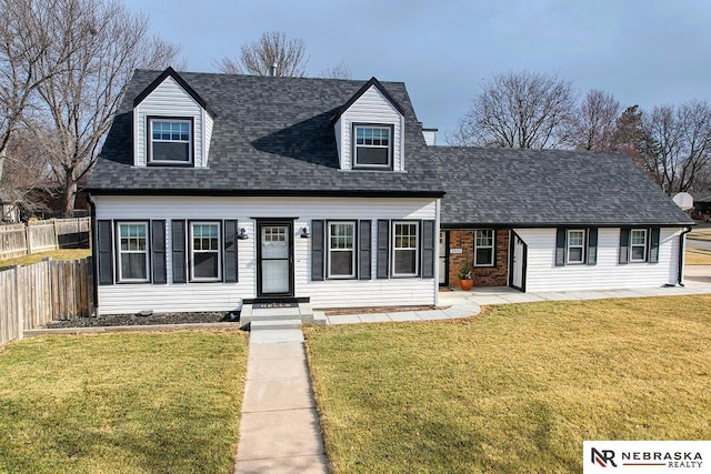 new england style home with a shingled roof, a front yard, brick siding, and fence