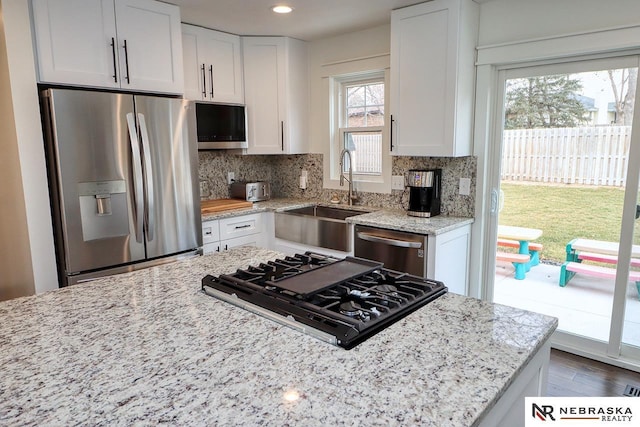 kitchen featuring stainless steel appliances, a sink, white cabinets, light stone countertops, and tasteful backsplash