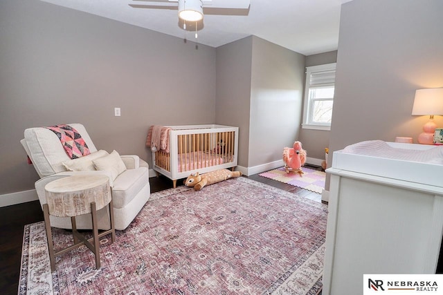 bedroom with a ceiling fan, a nursery area, and baseboards