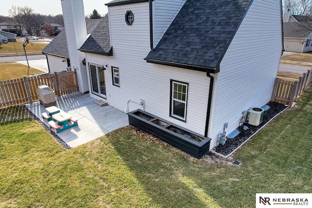 back of property featuring a shingled roof, a patio area, a lawn, and a chimney