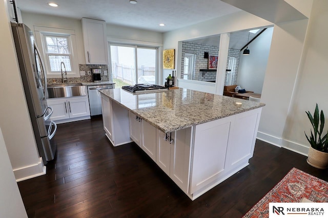 kitchen with light stone counters, a center island, stainless steel appliances, white cabinetry, and a sink