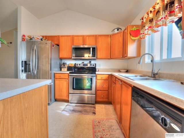 kitchen with lofted ceiling, a sink, light countertops, appliances with stainless steel finishes, and brown cabinetry