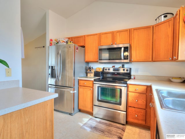 kitchen with stainless steel appliances, a sink, vaulted ceiling, light countertops, and brown cabinetry