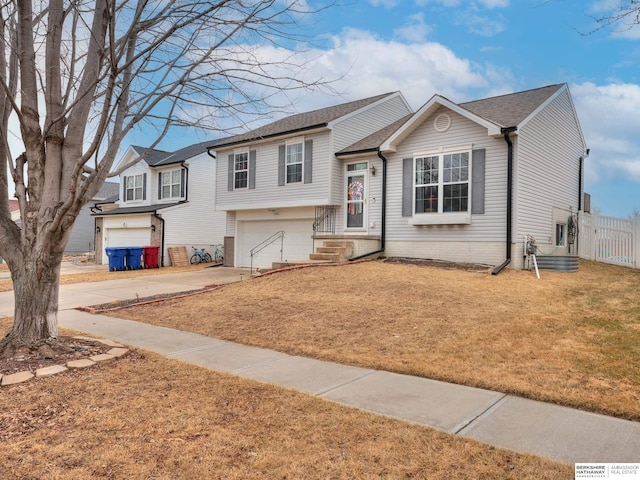 split level home featuring an attached garage, a front lawn, concrete driveway, and roof with shingles