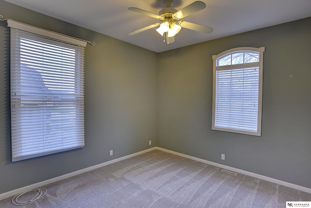 carpeted empty room featuring ceiling fan, visible vents, and baseboards