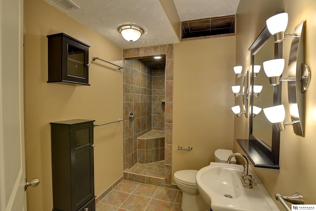 bathroom with visible vents, toilet, a tile shower, a textured ceiling, and tile patterned floors